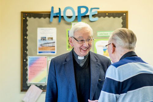 Clergyman and elderly gentleman talking under 'hope' sign